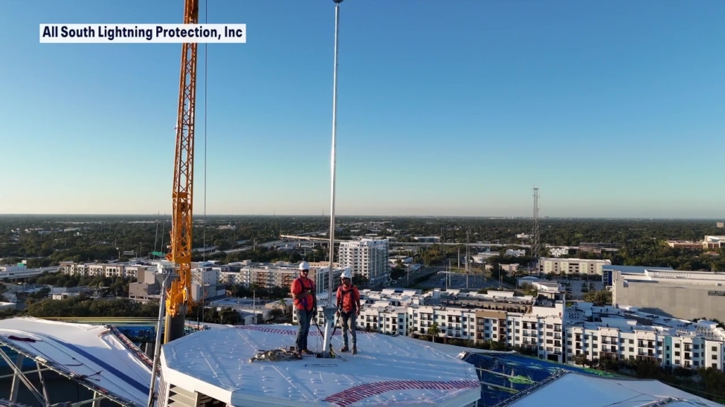 Two All South Lightning Protection installers standing beside a lightning rod on the roof of Tropicana Field in St. Petersburg